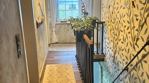 Un pasillo estrecho con piso de diseño geométrico, baranda de madera y pared con motivo de hojas.