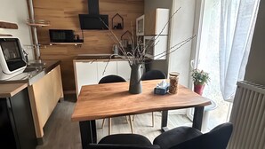Een moderne keuken met een houten tafel, stoelen, een vaas met takken, een pot met koekjes en een plant in pot.