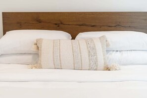 Un lit avec du linge de lit blanc, une tête de lit en bois et deux coussins décoratifs.
