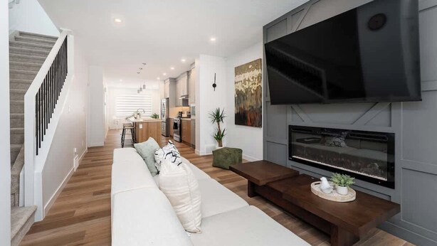 Ein modernes Wohnzimmer mit großem Flachbildfernseher, Kamin, einer Couch und einer Treppe.