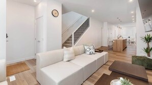 Ein modernes Wohnzimmer mit einem weißen Sofa, einer Treppe, einer Küchenzeile und einem Essbereich.