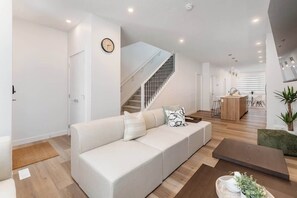 Ein modernes Wohnzimmer mit einem weißen Sofa, einer Treppe, einer Küchenzeile und einem Essbereich.