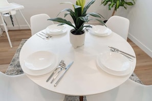 Une table de salle à manger ronde, avec de l’assiette blanche, des couverts et une plante en pot.