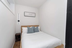 Ein Schlafzimmer mit einem Bett, einem Nachttisch, einer Wandleuchte und einem gerahmten Bild.