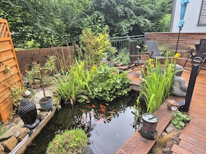 Ein Garten mit Teich, Holzterrasse und unterschiedlichen Pflanzen.