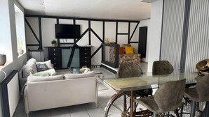 Un saló modern amb un sofà, taula de menjador, cadires, un televisor i una escala.