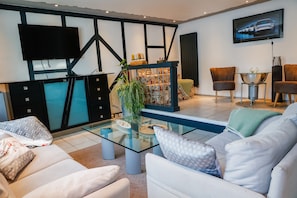 Ein modernes Wohnzimmer mit einem Glastisch, weißen Sofas, einem an der Wand befestigten Fernseher und einer Treppe mit dekorativer Geländer.