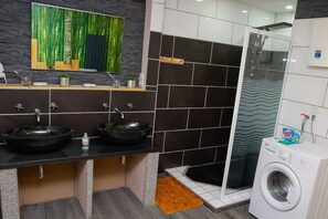 A modern bathroom with two sinks, a shower, and a washing machine.