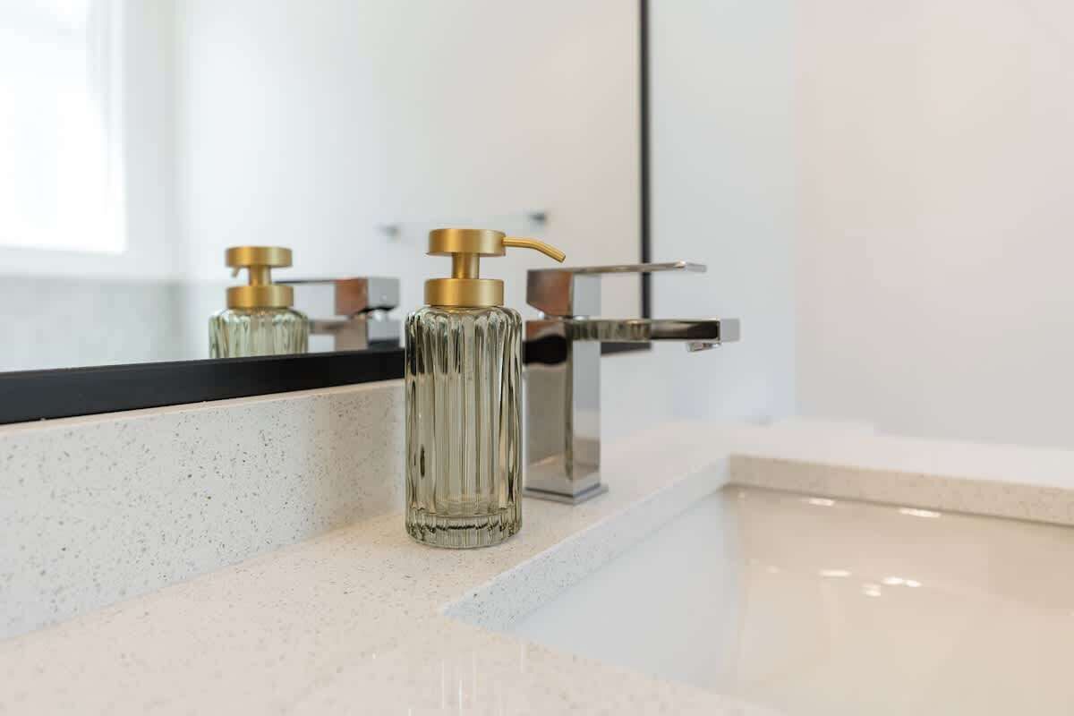 A bathroom with a modern faucet, a glass soap dispenser, and a reflective mirror.