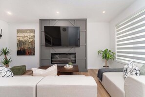 A modern living room with a flat-screen TV, a fireplace, and two sofas. - 3BR Home Near Rogers Place & NAIT with Garage Parking (Edmonton)