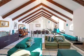 Ein großzügiges Loft mit hohen Decken, freiliegenden Holzbalken, einer Essecke und einer gemütlichen Sitzecke mit grünen Polstermöbeln.
