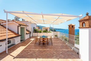 A terrace with a table and chairs, a white pergola, and a view of the sea. - YourHome - La Terrazza nel Blu (Piano di Sorrento)