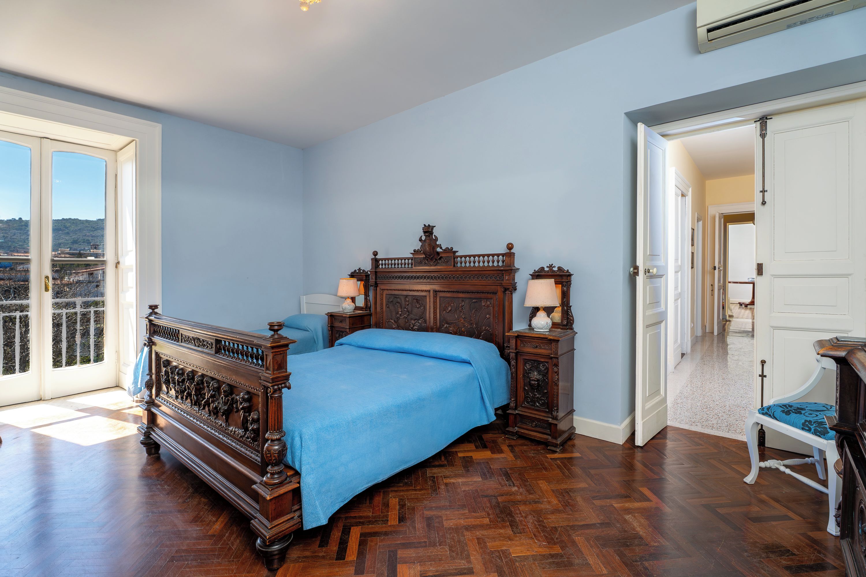 Un dormitorio con una cama grande, un aparador de madera, una silla y vistas por una puerta.