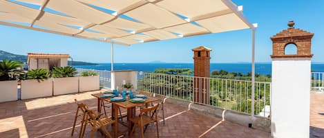 An outdoor patio with a table set for dining, overlooking a coastal view.