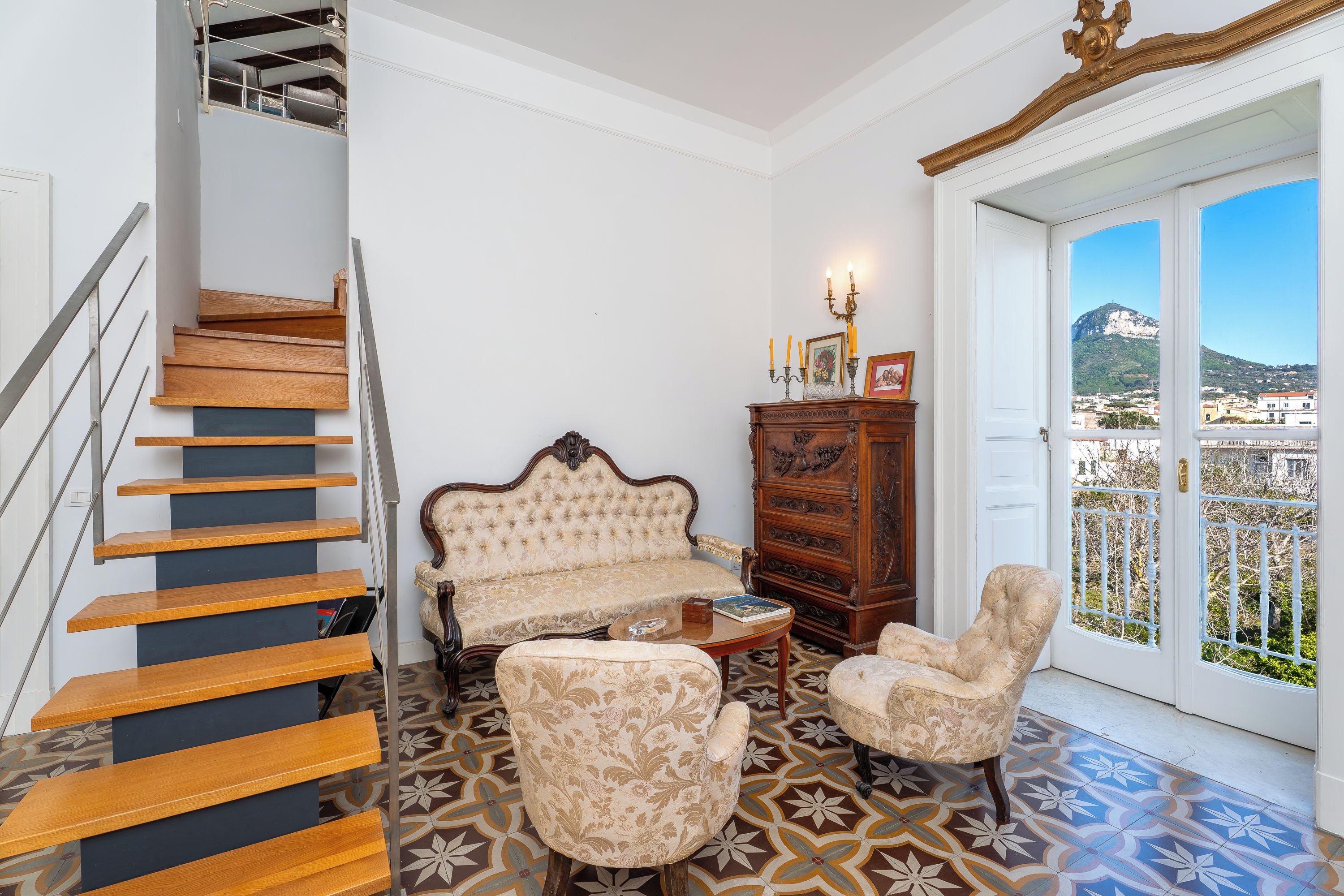 Eine Treppe mit Holzdielen, ein Sofa, zwei Sessel, ein Holzschrank und Blick durch eine Tür.
