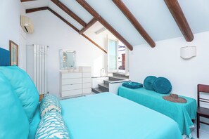 A bedroom with a sloped ceiling, a bed with teal bedding, a dresser, a chair, and a small table with a hat and pillow. - YourHome - La Terrazza nel Blu (Piano di Sorrento)