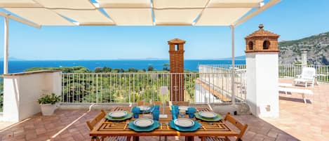 A terrace with a table set for dining, overlooking a coastal view.