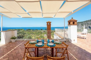 A terrace with a table set for dining, overlooking a coastal view. - YourHome - La Terrazza nel Blu (Piano di Sorrento)