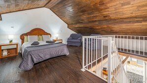 Quarto com teto de madeira, uma cama, uma cadeira e um corrimão branco.