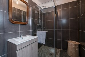 Casa de banho moderna com um espelho grande, uma pia, um chuveiro e um balde de madeira.