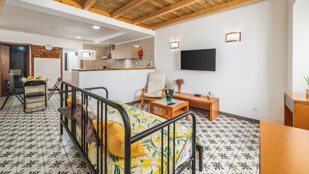 Quarto com cama, escrivaninha, cadeira, televisão e cozinha.