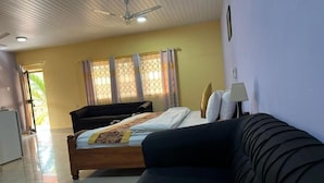 Una habitación con cama, sofá, ventilador de techo y ventana con cortinas.