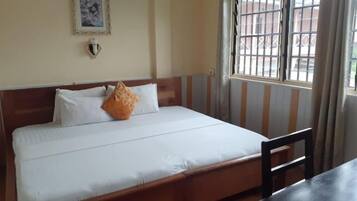 Una cama con cabecera de madera, una mesita de noche y una ventana con barrotes.