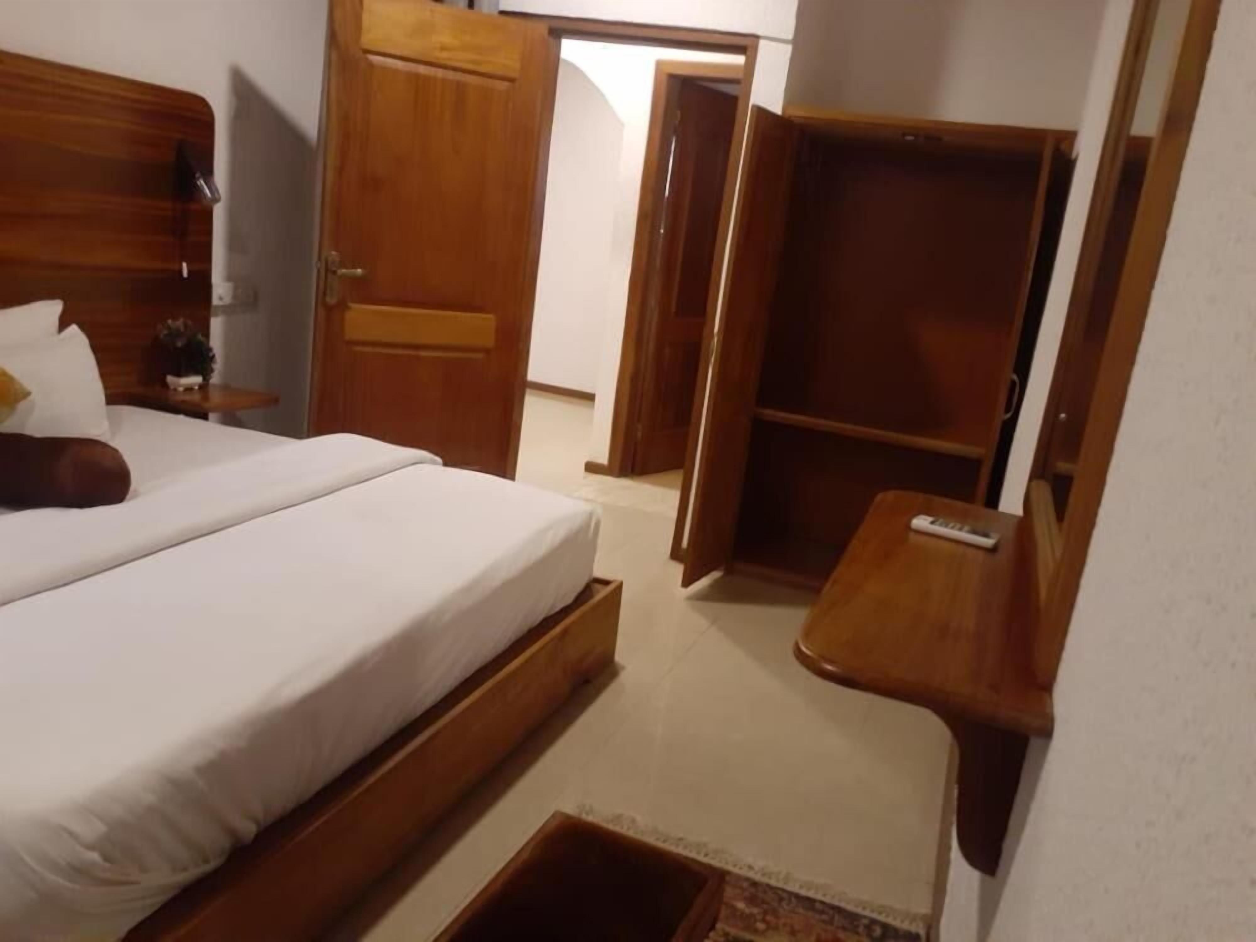A bedroom with a bed, wooden wardrobe, and a small bedside table.