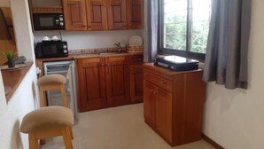 Cocina compacta con armarios de madera, microondas, tostadora y ventana con cortinas.