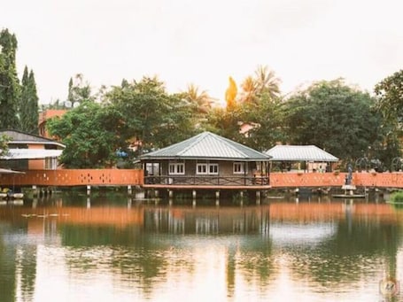 A building with a roof over water, surrounded by trees and a fence.