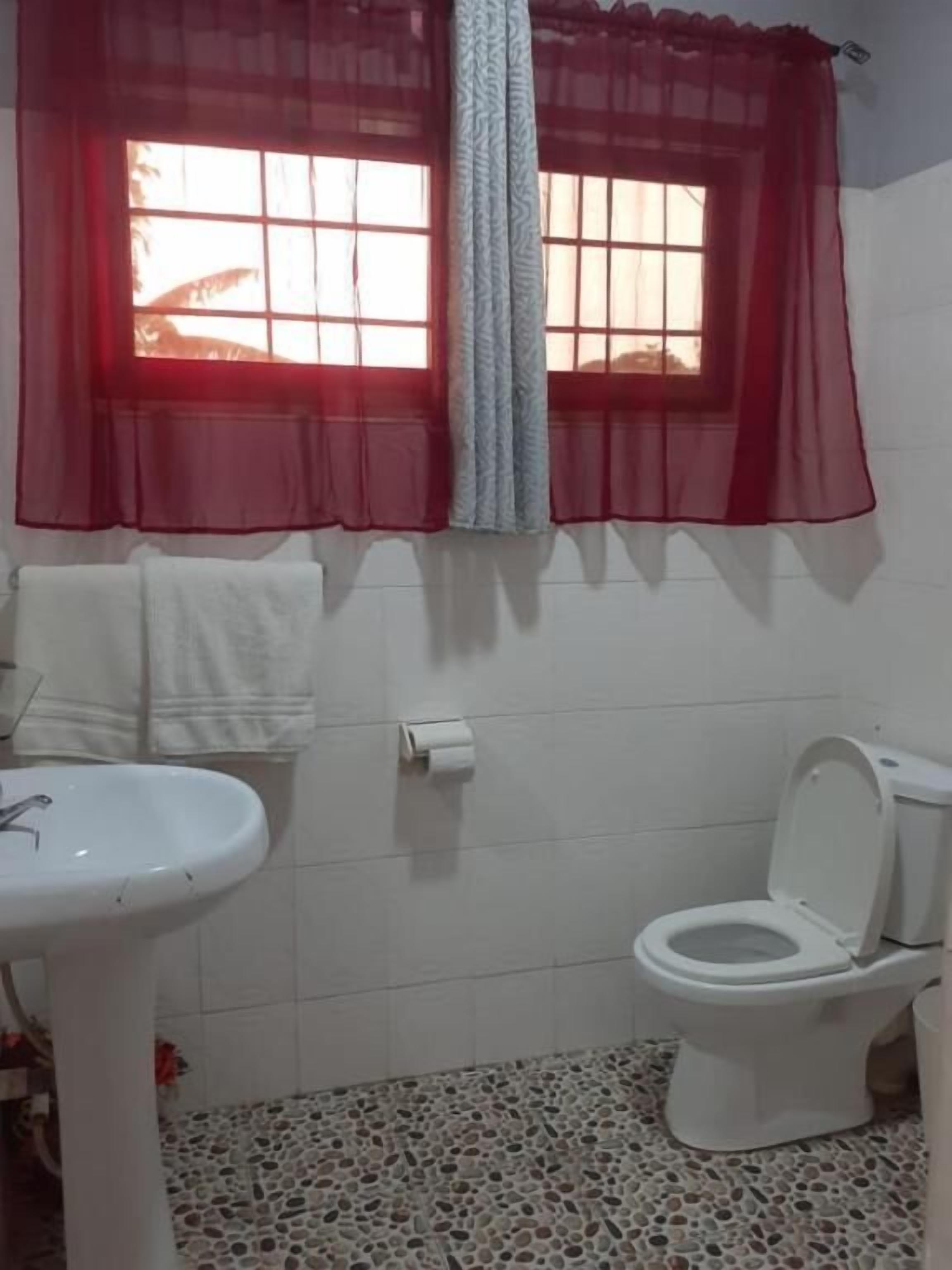 Un bagno con un lavandino, un water e una finestra con tende rosse.
