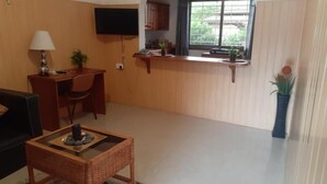 Una sala de estar con televisión, escritorio, silla, mesa de centro y ventana con vistas.