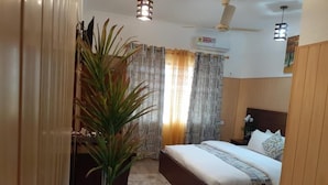 Un dormitorio con cama, cortinas, una planta en maceta y un ventilador de techo.