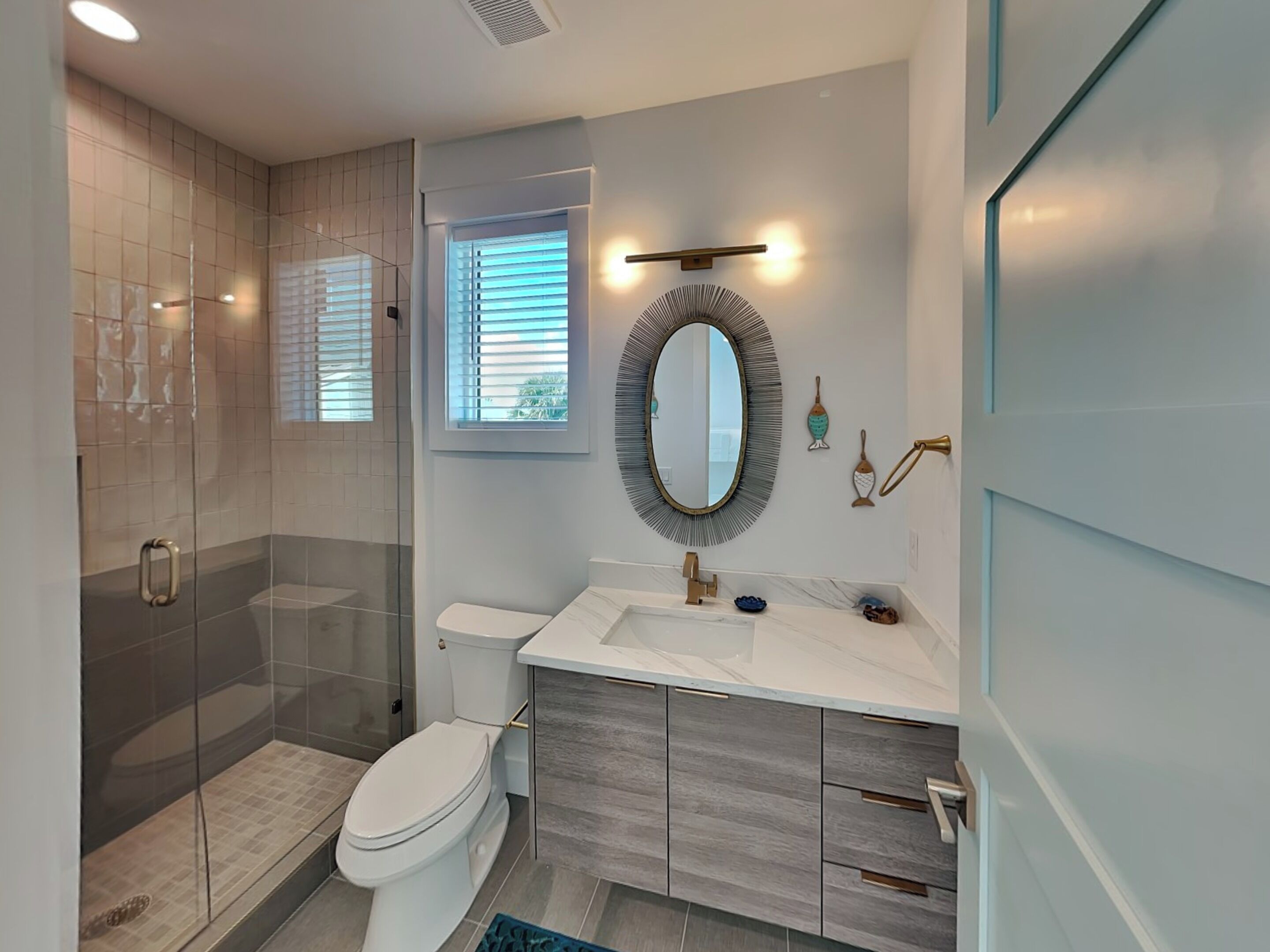 A modern bathroom with a glass-enclosed shower, a toilet, a vanity with a marble countertop, and a large mirror.