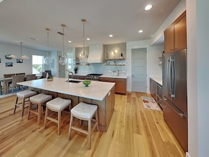 A modern kitchen with a central island, bar stools, stainless steel appliances, pendant lighting, and wooden flooring. - Ocean Retreat (St. Augustine)