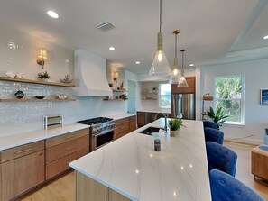 A modern kitchen with a central island, stainless steel appliances, and pendant lighting. - Ocean Retreat (St. Augustine)
