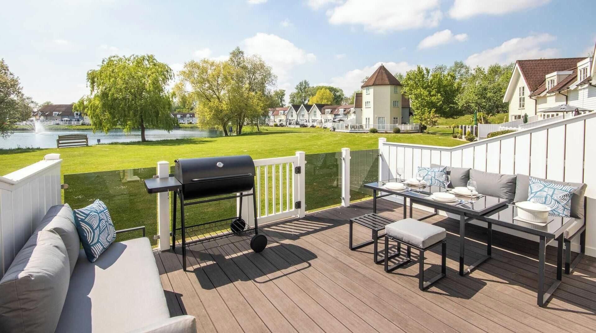 En terrasse med grill, udendørs møbler og udsigt til et sø og huse.
