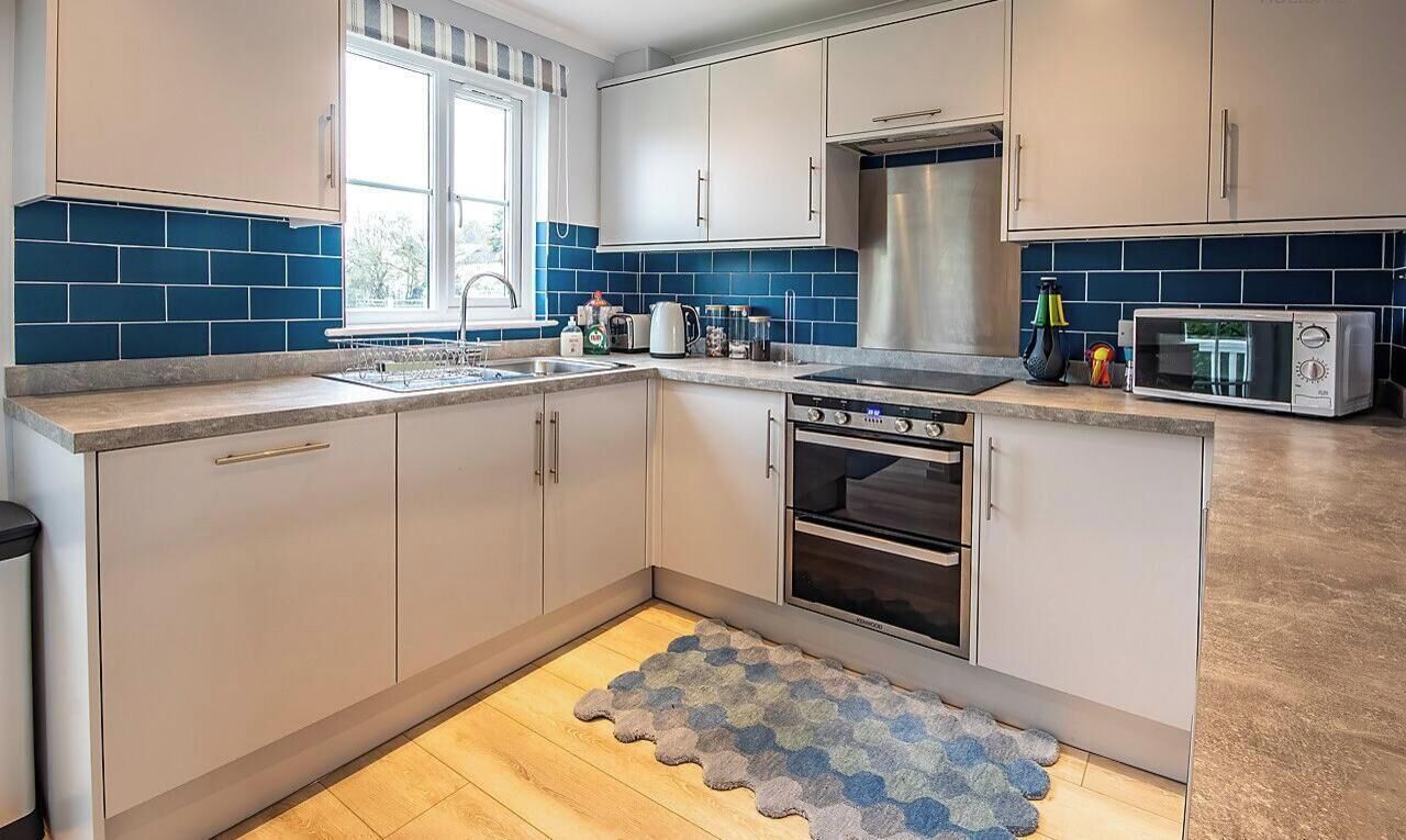 A modern kitchen with white cabinets, a stainless steel refrigerator, a microwave, and a built-in oven.