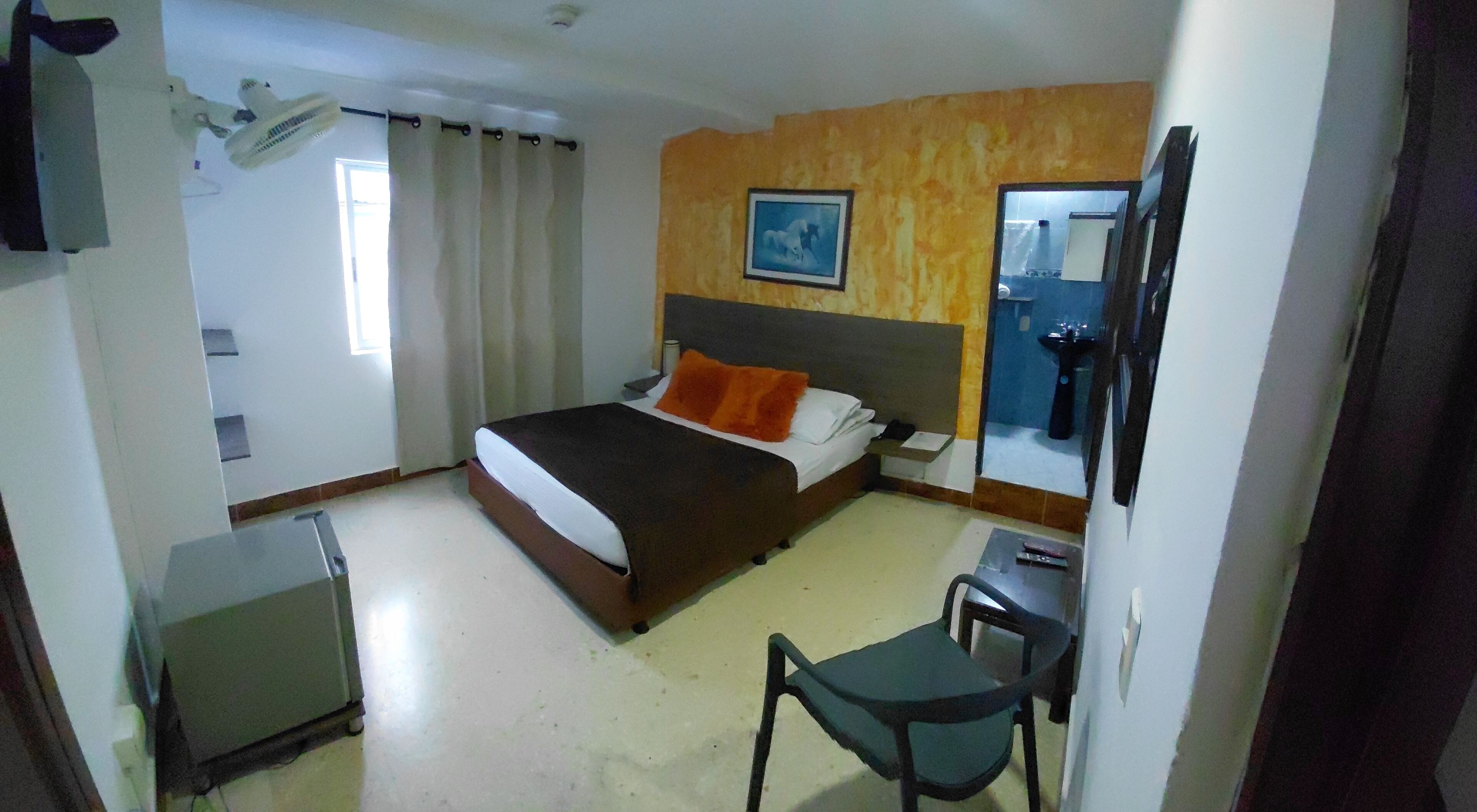 Habitación de hotel con cama, escritorio, silla, espejo y ventana con cortinas.