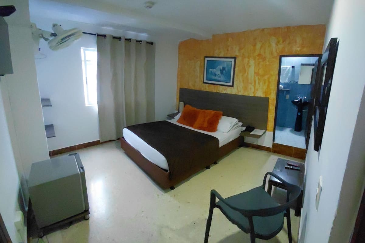 Une chambre d’hôtel avec un lit, un bureau, une chaise, un miroir et une fenêtre avec des rideaux.
