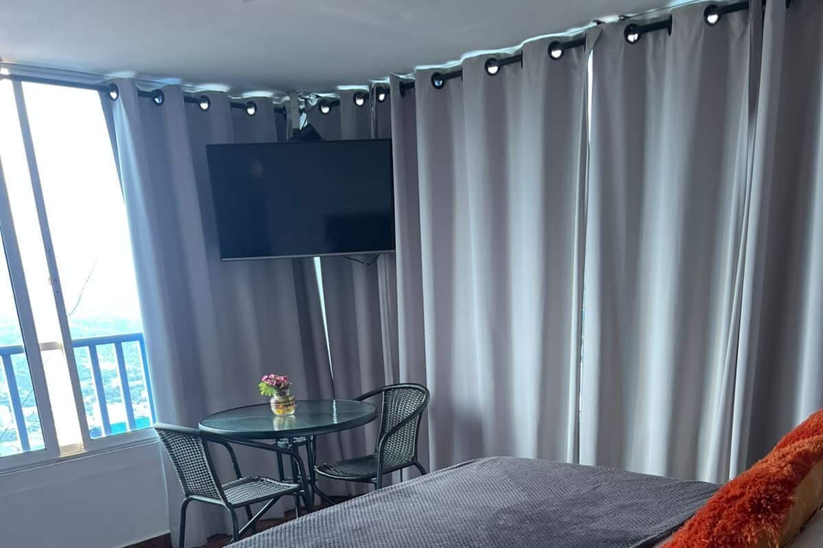 Une chambre d’hôtel avec un lit, une table et des chaises, une télévision et un balcon avec des rideaux.