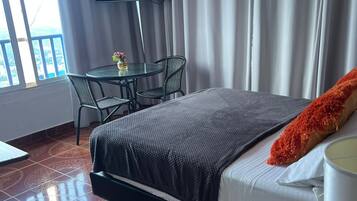 Una camera d'albergo con un letto, un tavolo con sedie, una televisione e un balcone con tende.