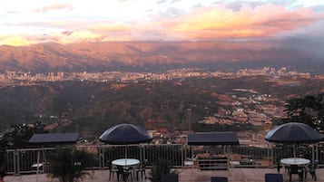 A terrace with outdoor seating and a view of a cityscape and mountains.