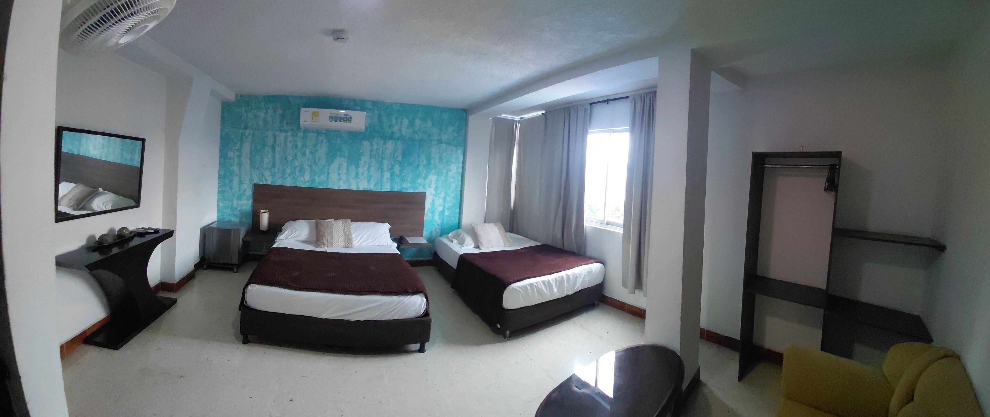 Habitación de hotel con dos camas, una mesita de noche, una silla, un escritorio, un espejo y una ventana con cortinas.