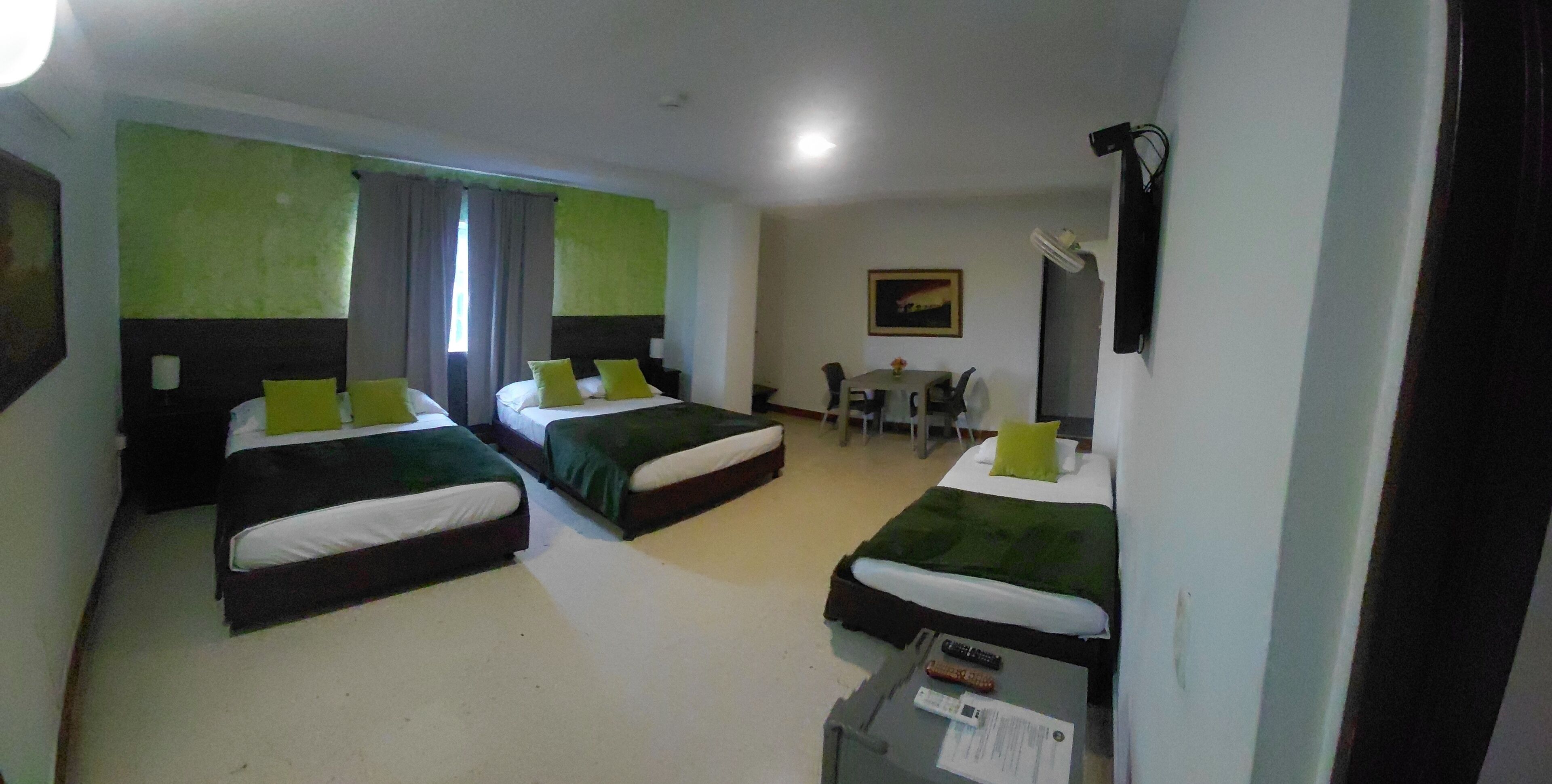 Habitación de hotel con tres camas, un escritorio, una silla, una mesa y un cuadro en la pared.