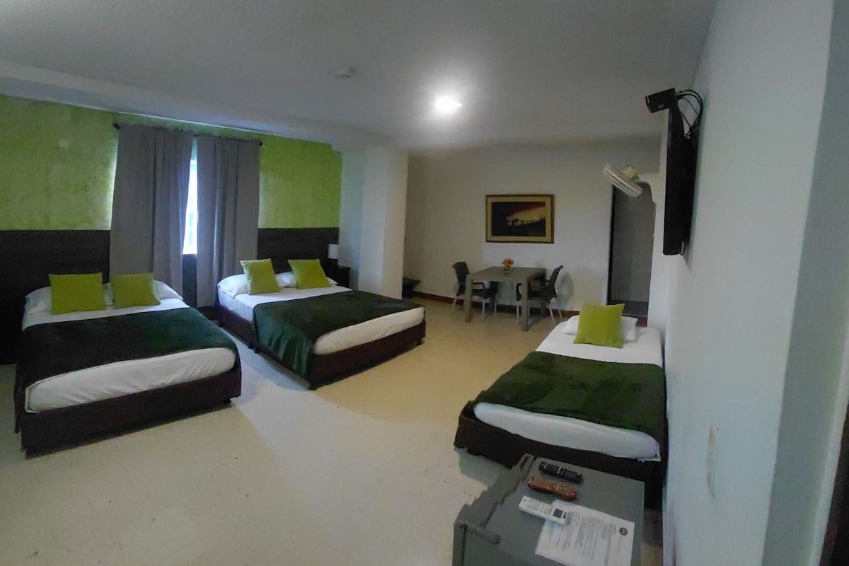 Une chambre d’hôtel avec trois lits, un bureau, une chaise, une table et un tableau au mur.