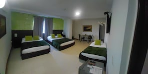 Habitación de hotel con tres camas, un escritorio, una silla, una mesa y un cuadro en la pared.