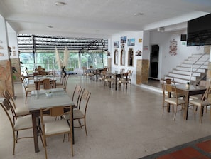 Un vaste espace dédié à la salle à manger, avec de nombreuses tables et chaises, de grandes fenêtres et un escalier.
