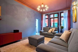 En moderne stue med et rødt skab, grå sofaer og en markant lampe.
