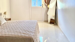 Ein Schlafzimmer mit einem Bett, einer Deckenleuchte, einem Fenster mit Vorhängen, einem wandmontierten Spiegel und einer Tür.